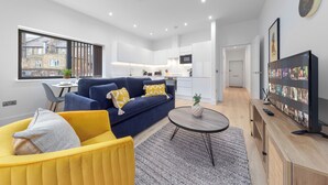 A modern living room with a blue sofa, yellow armchair, and a flat-screen TV.