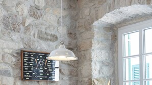 Un coin repas avec un mur en pierre, une table en bois, des chaises noires, un luminaire suspendu et une maquette de voilier décorative.