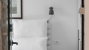 Un lit bien fait, avec des draps blancs et des serviettes pliées, une lampe de chevet et un tableau encadré au mur.