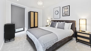 A modern bedroom with a large bed, bedside tables, a wardrobe, and artwork on the walls. - Bejoux Court - Apt 1 (Harrow)