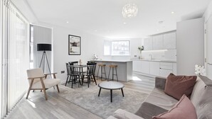 A modern living room with a sofa, a coffee table, and a dining area with chairs and a table. - Bejoux Court - Apt 1 (Harrow)