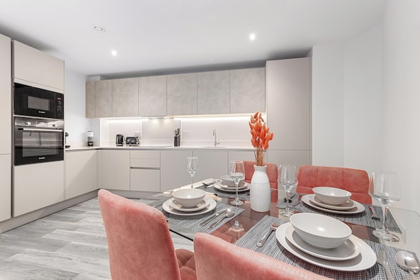 A modern kitchen with built-in appliances, a dining area with pink chairs, and a central island with a vase.