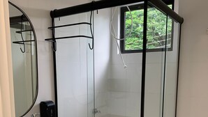 Moderni kylpyhuone, jossa on lasiseinällä varustettu suihku, valkoinen pesuallas ja wc.