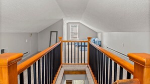 Eine Treppe mit hölzernen Geländern und schwarzen Spindeln, die zu einem Schlafzimmer mit Fenster und Bett führt.