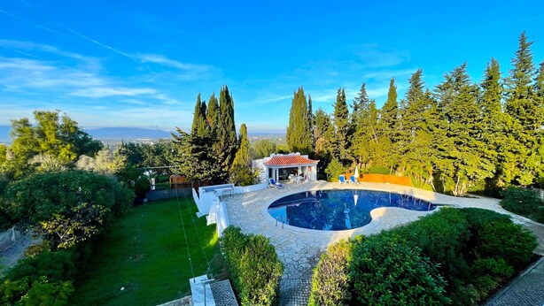 A pool surrounded by a stone patio, a small gazebo, and tall trees. - Villa Mandarin (Carvoeiro)