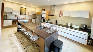 A modern kitchen with a central island, bar stools, stainless steel appliances, and white cabinetry. - Villa Mandarin (Carvoeiro)