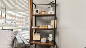 A modern living room with a leather sofa, a wooden bookshelf, and a window with blinds.
