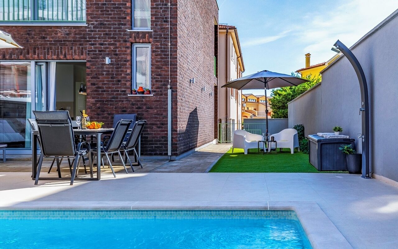 En swimmingpool med ett uteområde, en byggnad i tegel och en liten gräsmatta.