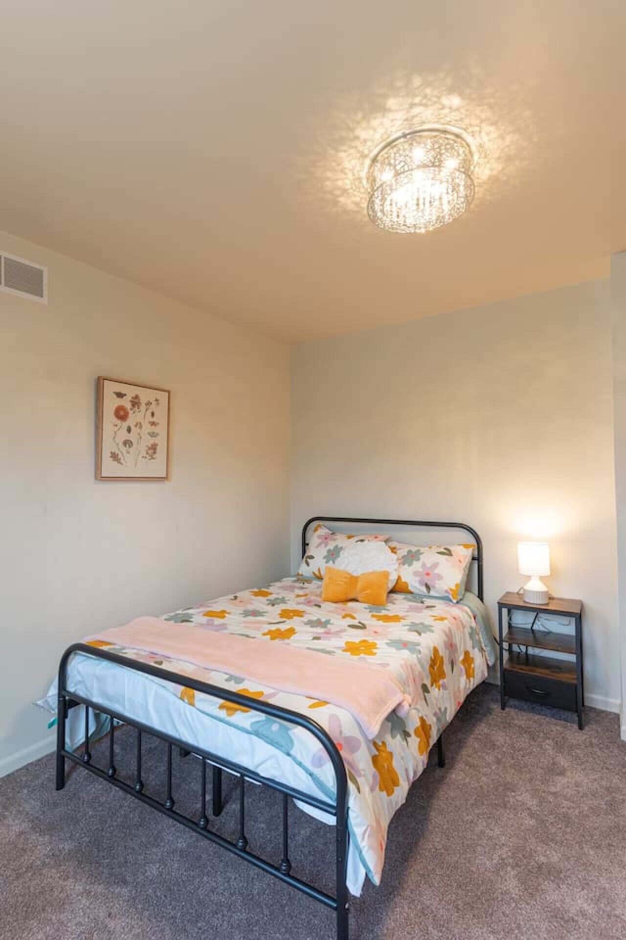 A bedroom with a bed, bedside table, lamp, and a wall decoration.