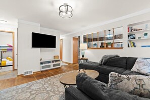 A modern living room with a flat-screen TV, grey sofa, and a coffee table. - Charming Home Near Target and Parks  2 Bathrooms (Dearborn Heights)