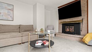 Un salon comprenant un canapé, une table basse en verre avec des livres, une cheminée et un téléviseur fixé au mur.