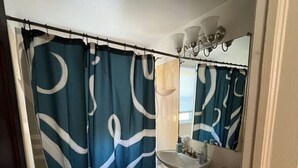 Un baño con bañera, inodoro, lavabo y cortina de ducha con un diseño ondulado.