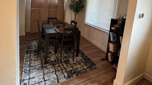 Un comedor con una mesa lista para cuatro personas, una alfombra y una estantería.