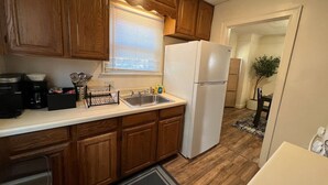 Una cocina compacta con armarios de madera, un lavamanos de acero inoxidable, un refrigerador blanco y una ventana con persianas.