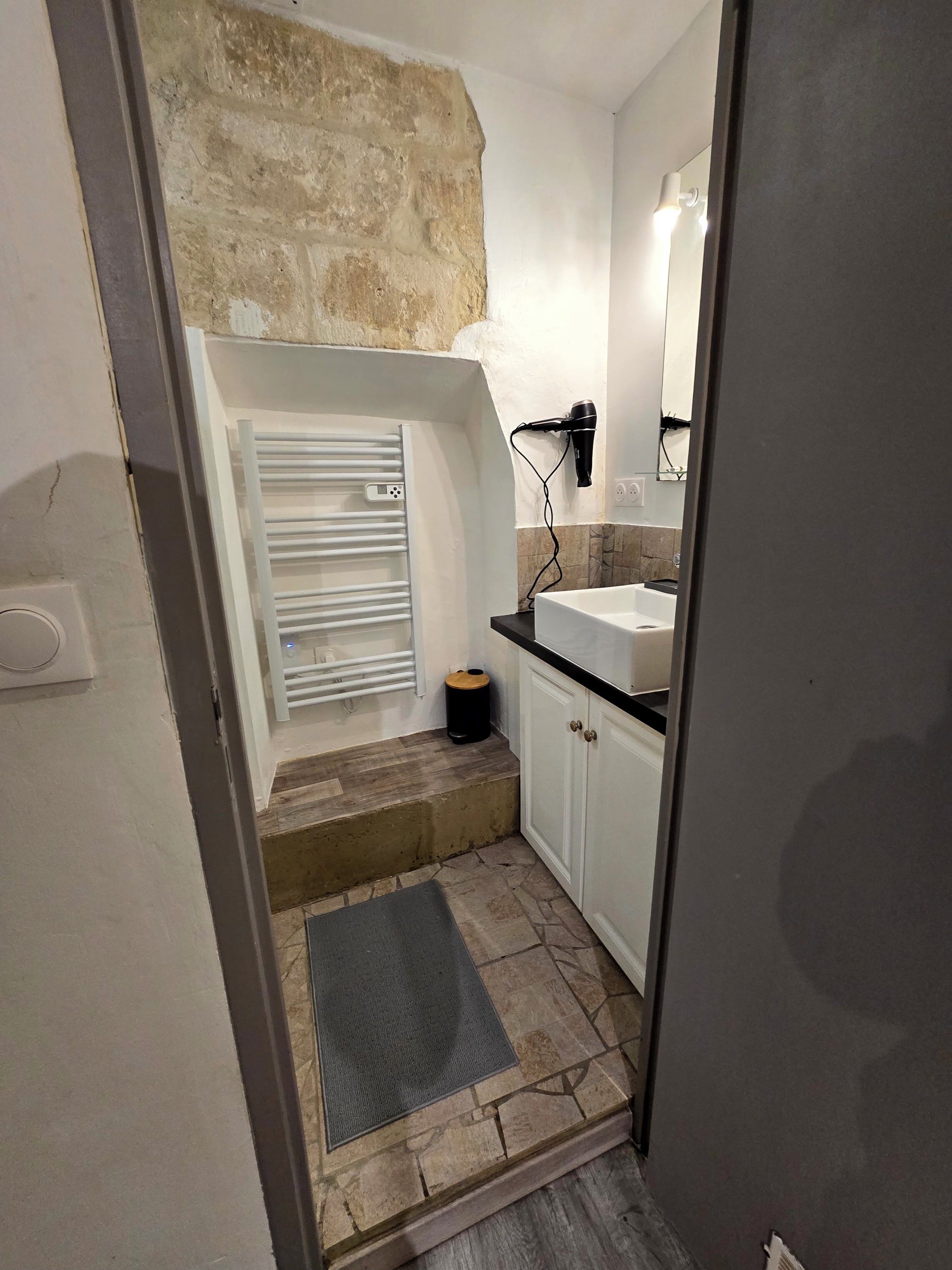 Une petite salle de bain avec un mur en pierre, un lavabo blanc, un miroir et un porte-serviettes.