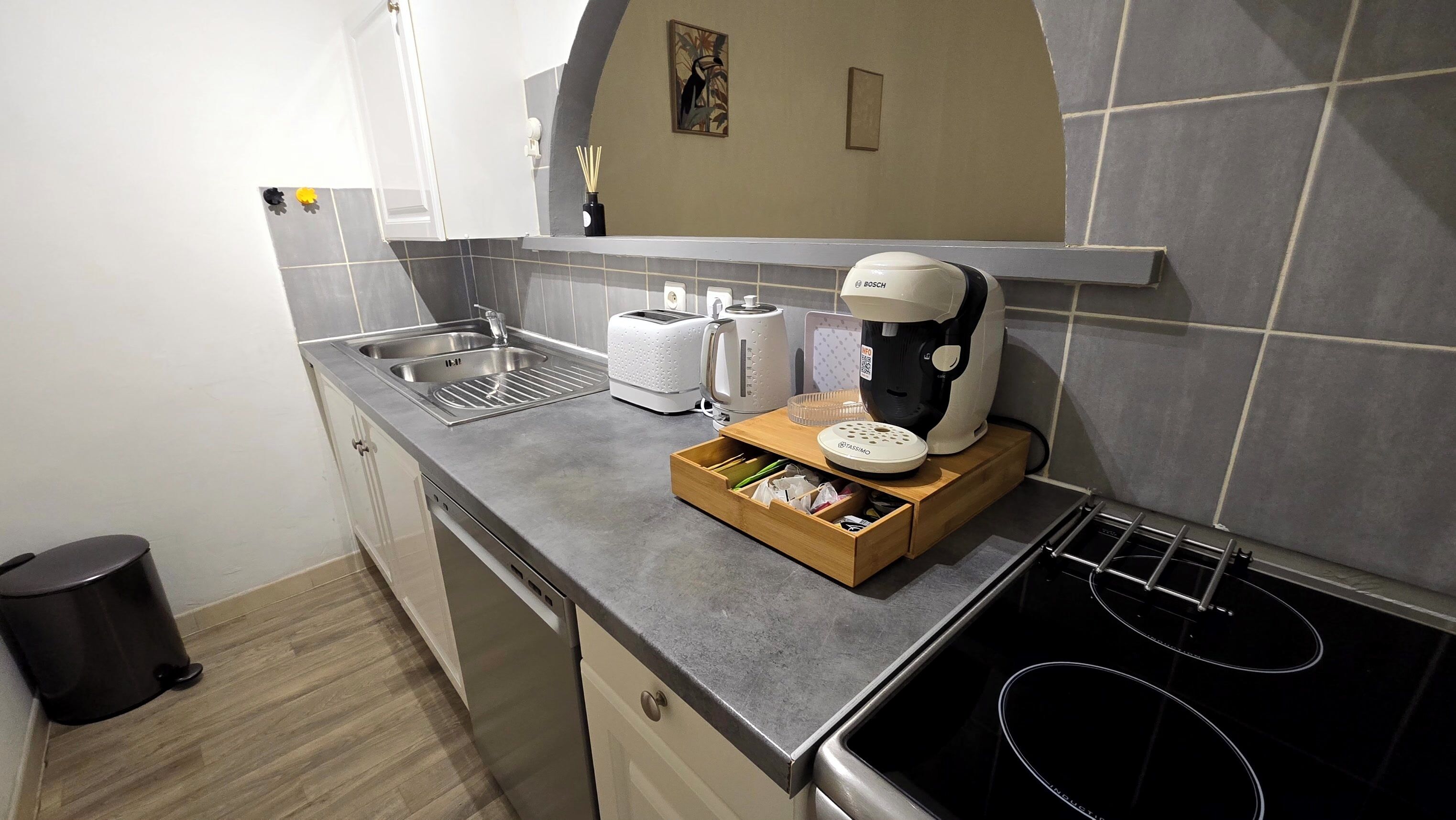 Uma cozinha compacta com pia, torradeira, cafeteira e uma pequena caixa de madeira.