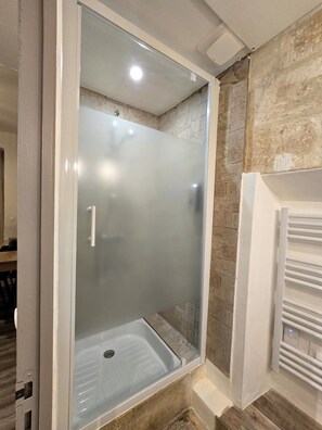 A glass-enclosed shower with a white frame, stone wall, and a white towel rack. - 60m² apartment in a historic and authentic environment (Beaucaire)