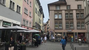 A street with buildings, outdoor seating, and pedestrians.
