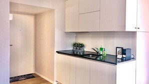 A modern kitchen with white cabinets, a black countertop, and a built-in sink. There are small potted plants on the counter and a coffee machine.