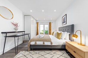 A modern bedroom with a bed, bedside table, lamp, and a view of the outdoors. - The Hyde - Apt 5 (London)