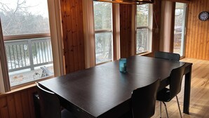 Interior de madera con una mesa y sillas de madera oscura, ventanas grandes y un reloj en la pared.