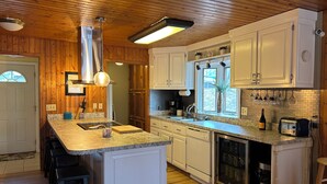 Una cocina con paneles de madera, gabinetes blancos, encimera de granito, lavavajillas integrado y una ventana con vistas.