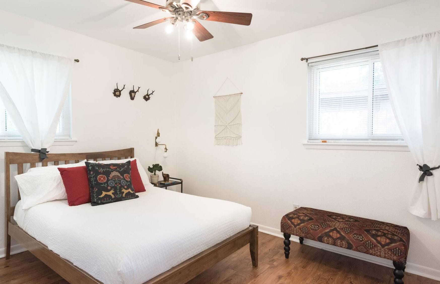 A bedroom with a wooden bed, a bench, a ceiling fan, and a window with curtains.
