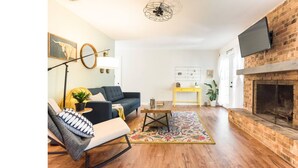 A living room with a sofa, a coffee table, a fireplace, and a TV mounted on the wall. - Woodstone Getaway (Austin)