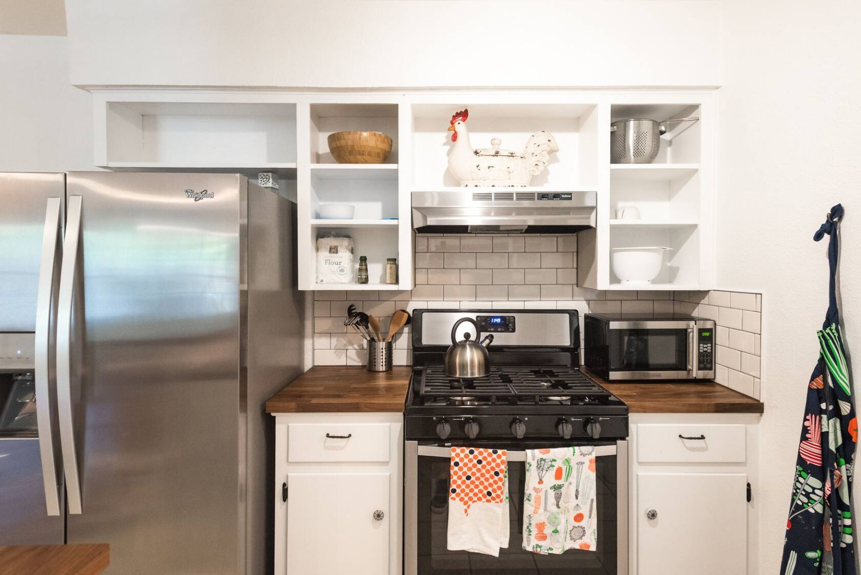 A modern kitchen with a stainless steel refrigerator, a gas stove, a microwave, and white cabinetry.