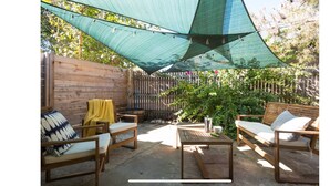 An outdoor patio area with wooden furniture, a table, and a green shade sail. - Woodstone Getaway (Austin)