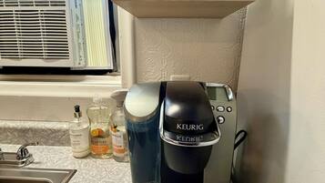 Eine Küchenzeile mit einer Keurig-Kaffeemaschine, einem Spülbecken und einem Fenster mit Klimaanlage.