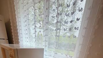 Ett kök med en mikrovågsugn, ett träskåp med lådor, en skål på bänkskivan och ett fönster med blommiga gardiner.