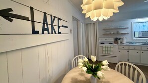 Comedor con una mesa, sillas, un jarrón de flores, un cartel en la pared y una cocina al fondo.