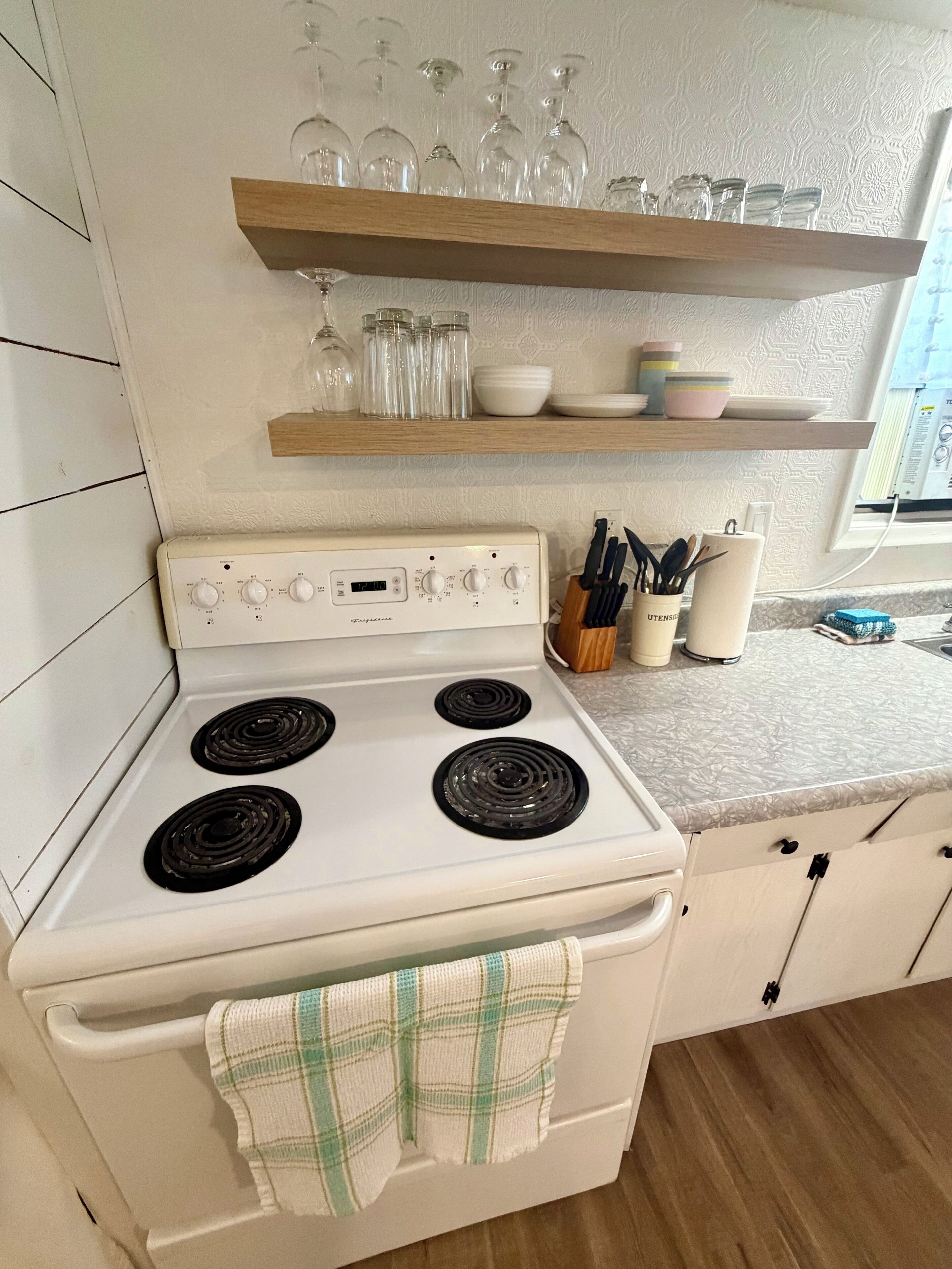 A kitchen with a white stove, wooden shelves above, and a window.