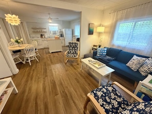 Un salon avec un canapé, une table à manger avec des chaises, un coin cuisine et une fenêtre avec des rideaux.