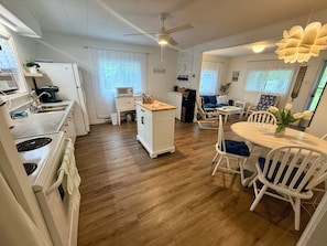A compact kitchen with a microwave, stove, and sink. There is a dining area with a table and chairs, and a ceiling fan. - Lake Mushamush Cottage! (Lower Northfield)