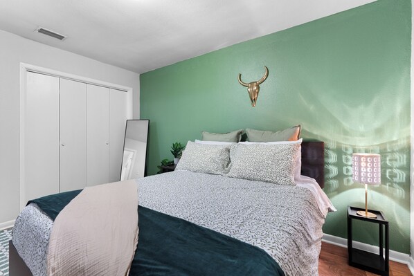 A bedroom with a green wall, a bed with patterned bedding, a bedside lamp, and a decorative bull skull.