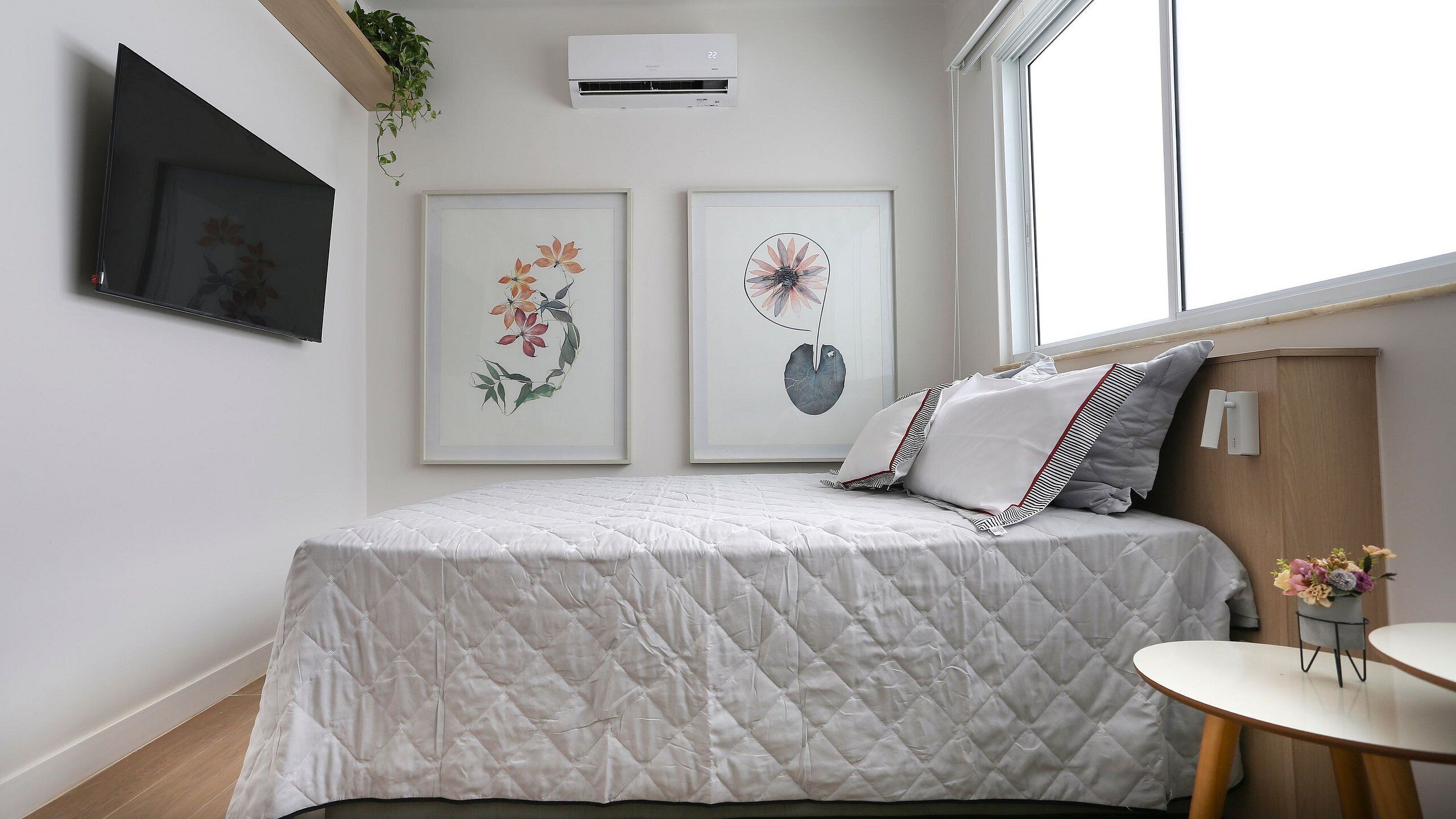 Ein Schlafzimmer mit einem Bett, zwei gerahmten Blumenbildern, einem kleinen runden Tisch und einem Blumentopf.