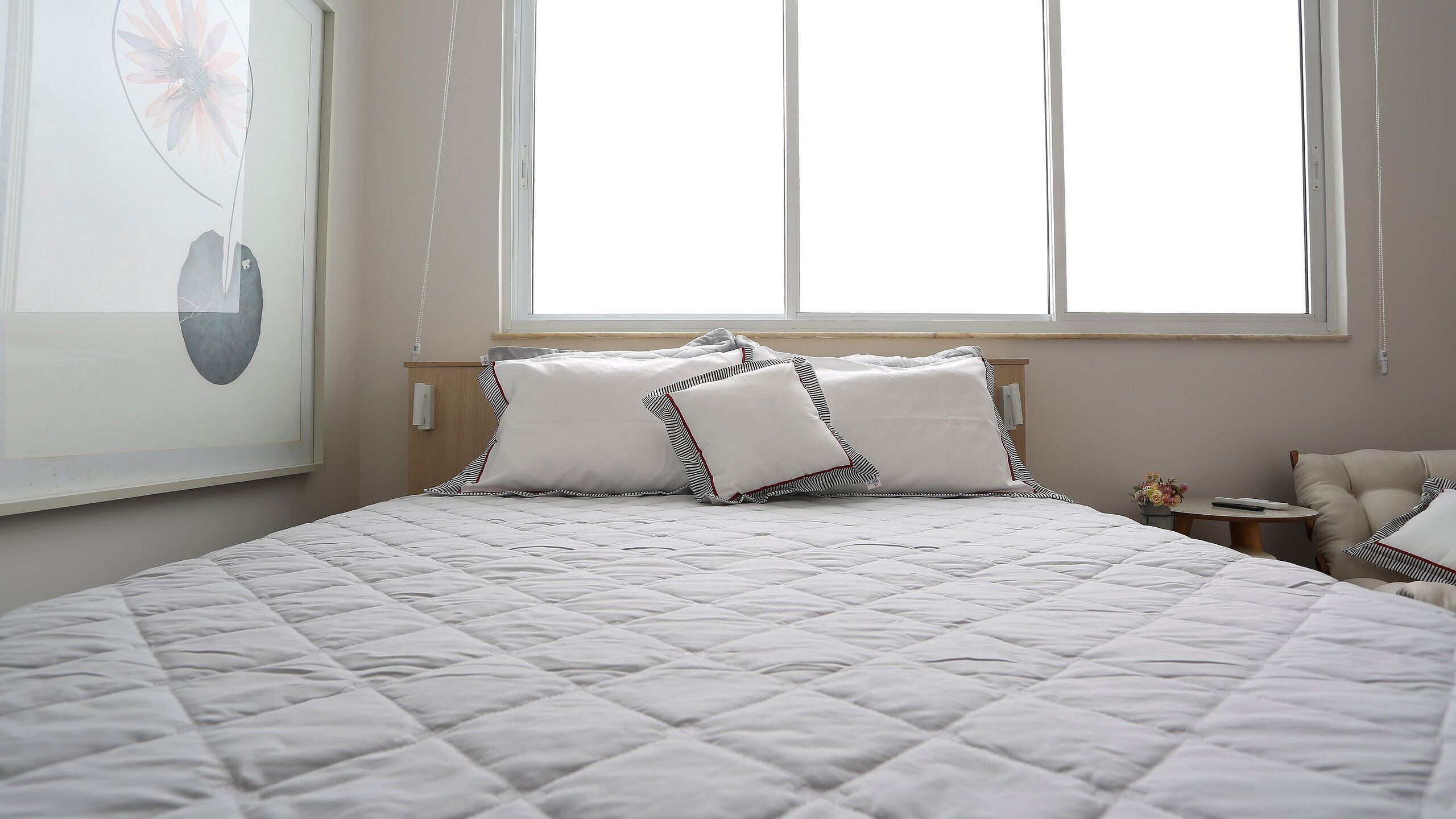 A neatly made bed with a quilted white duvet, two striped pillows, and a wooden headboard.