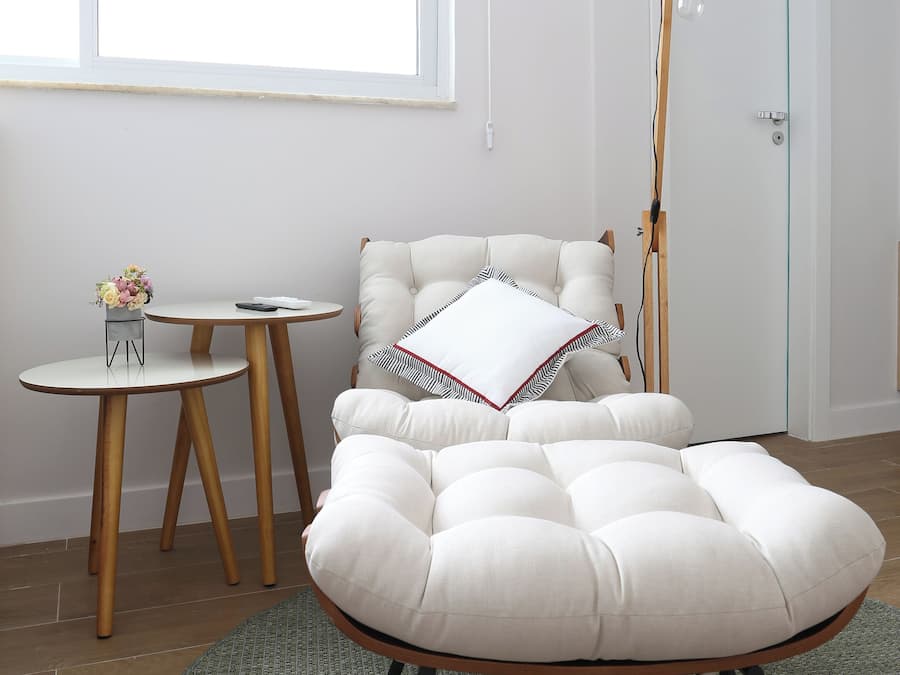 Un salon moderne avec un pouf capitonné, une table basse ronde et une petite table d’appoint sur laquelle est posé un vase de fleurs.