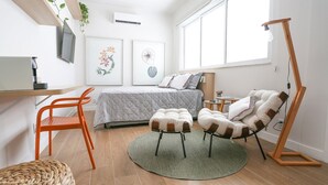 Ein modernes Schlafzimmer mit Bett, Schreibtisch, Stuhl, Stehlampe und Kunstwerken an den Wänden.