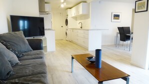 A modern living room with a grey sofa, a flat-screen TV, and a wooden coffee table. - 75 metres from small safe beach.  Sunsets to die for    (Auckland)