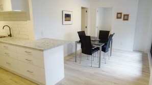 A modern kitchen with a marble countertop, a built-in sink, and a dining area with a glass table and black chairs. - 75 metres from small safe beach.  Sunsets to die for    (Auckland)