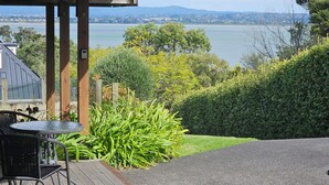 A patio with a table and chairs, a view of a lake, and a distant cityscape. - 75 metres from small safe beach.  Sunsets to die for    (Auckland)