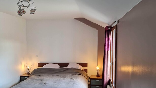 A bedroom with a bed, bedside tables, a nightstand, a radiator, and a window with curtains.