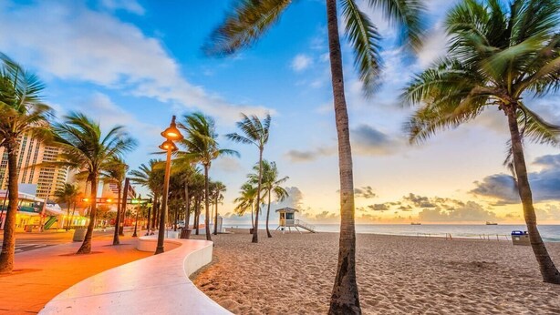 A beach with palm trees, a walkway, and a building in the background. - Villa #8 Pompano Beach: Spacious 1BR Canal View 4 Min Walk to Beach (Pompano Beach)