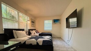 A bedroom with a bed, a desk, a chair, a TV, and two windows with blinds. - Villa #8 Pompano Beach: Spacious 1BR Canal View 4 Min Walk to Beach (Pompano Beach)
