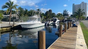 A marina with boats docked, a wooden walkway, and palm trees. - Villa #8 Pompano Beach: Spacious 1BR Canal View 4 Min Walk to Beach (Pompano Beach)