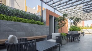 Une terrasse extérieure avec des sièges, une pergola et un jardinier avec des plantes.