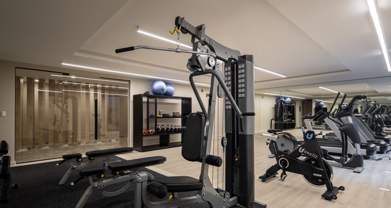 Un gimnasio con máquinas de cardio, equipo de levantamiento de pesas y un espejo grande.
